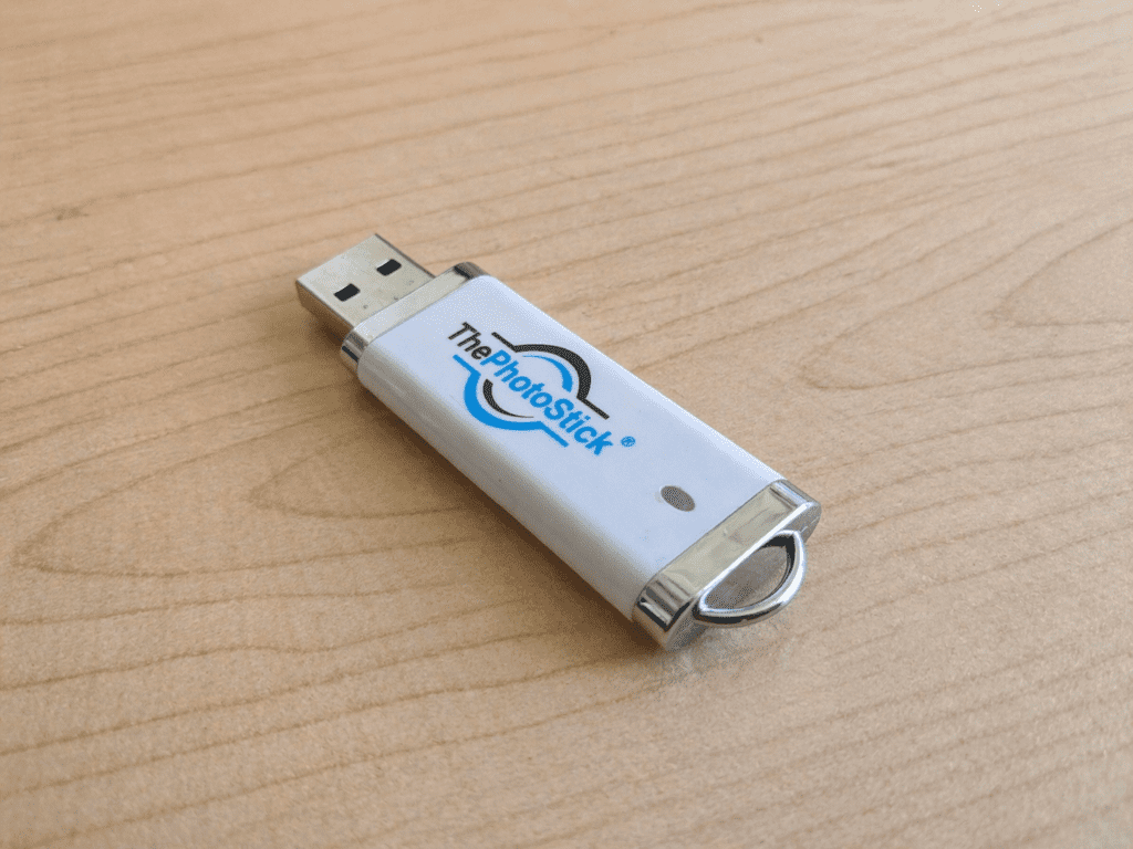 Thephotostick Review 2026: Is It A Scam Or Legit? 14 PhotoStick review close-up: Silver 128GB device unboxed on a wooden desk.