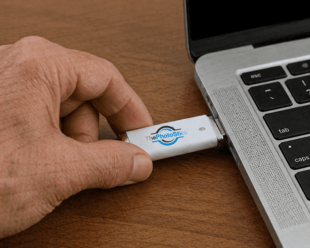 Thephotostick Review 2026: Is It A Scam Or Legit? 15 User testing ThePhotoStick review: Aged hand inserting the silver USB drive into a laptop port.
